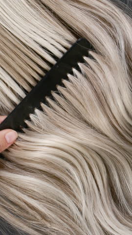 Vertical blond hair texture, slow motion of female hand combing long curly hair