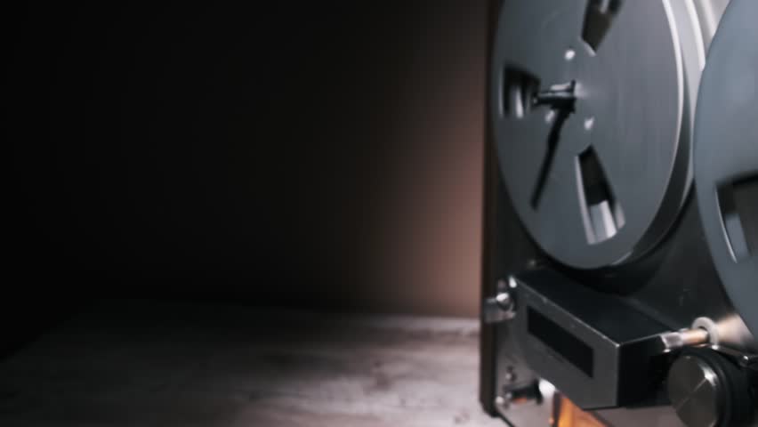 Close-up of a vintage reel-to-reel audio tape recorder in a dimly lit studio, highlighting its metallic reels and retro design. The composition evokes a sense of nostalgia and classic audio technology