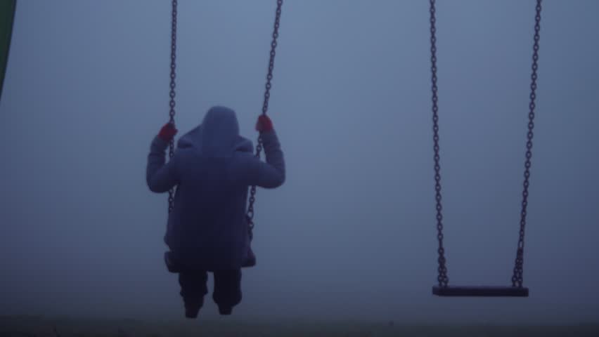 Woman sits on children swings in eerie dark foggy playground medium zoom shot selective focus