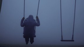 Woman sits on children swings in eerie dark foggy playground medium zoom shot selective focus - Powered by Shutterstock - Get 15% off with code: PIKWIZARD15