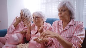 Senior women in pink colored pajamas making a pajama party at home. Watching tv series on the couch while eating popcorn. - Powered by Shutterstock - Get 15% off with code: PIKWIZARD15