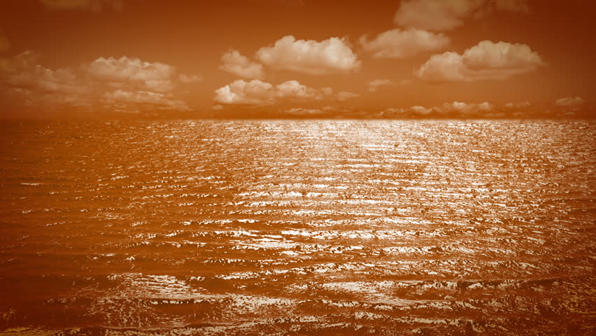 Ripples on the orange sea surface. Orange clouds moving fast on orange sky