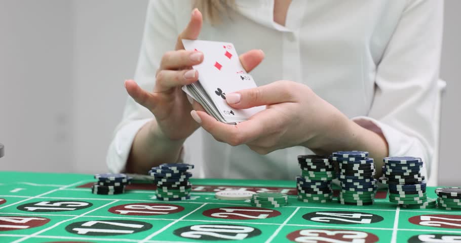 Woman shuffles playing cards sitting at gaming table. Female player in shirt prepares deck for next round of gambling game in casino slow motion
