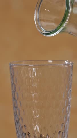freshly made yellow orange and mango smoothie flows into a glass from a bottle on a sunny yellow background