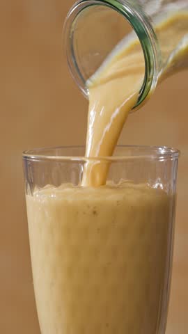 freshly made yellow orange and mango smoothie flows into a glass from a bottle on a sunny yellow background