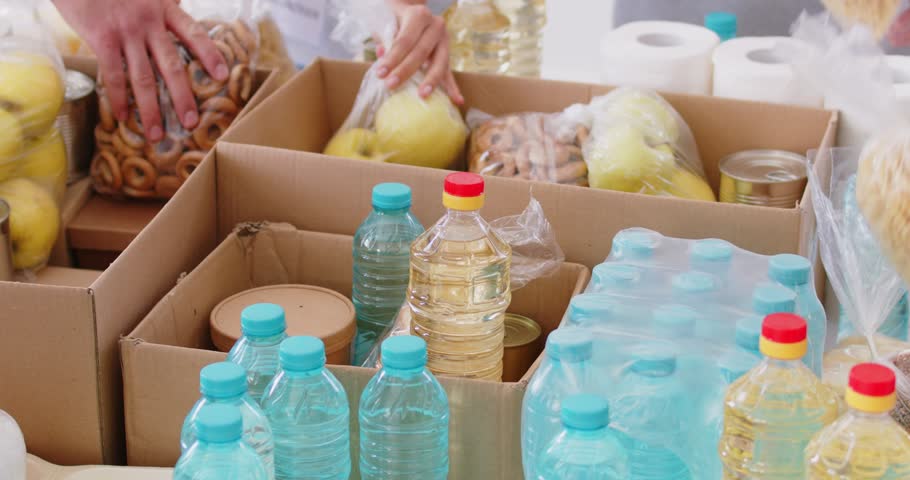 Group of volunteers preparing free food donations of foodstuffs in cardboard boxes for poor people. Charity workers working together in charitable foundation. Humanitarian aid concept. 4k video.