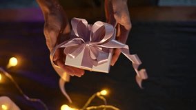 Pink ribbon wrapping gift box, soft string lights glowing, evoking warm holiday preparation scene - Powered by Shutterstock - Get 15% off with code: PIKWIZARD15