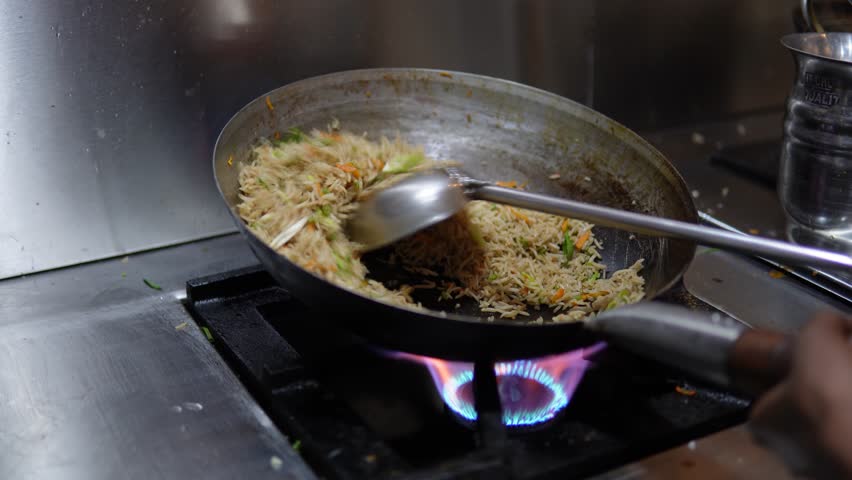 Cooking fried rice by flipping and stirring in the wok on the gas stove in Delhi