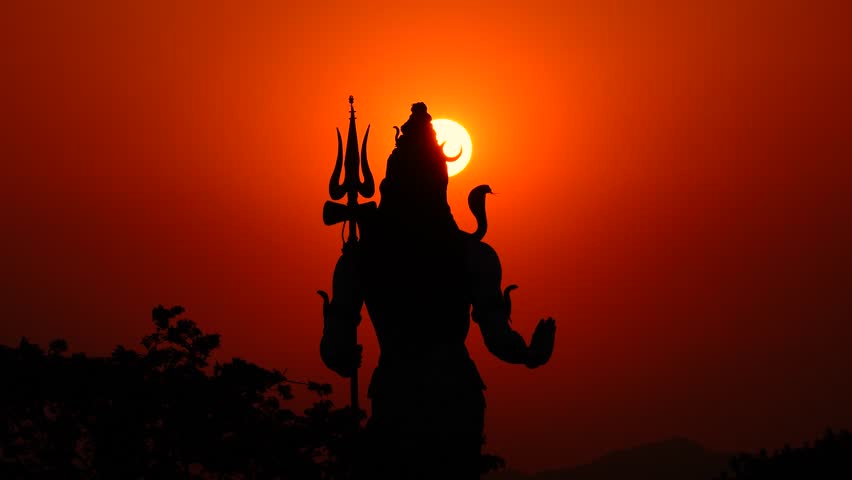Focusing on the silhouetted Lord Shiva at sunrise in the orange Haridwar sky.