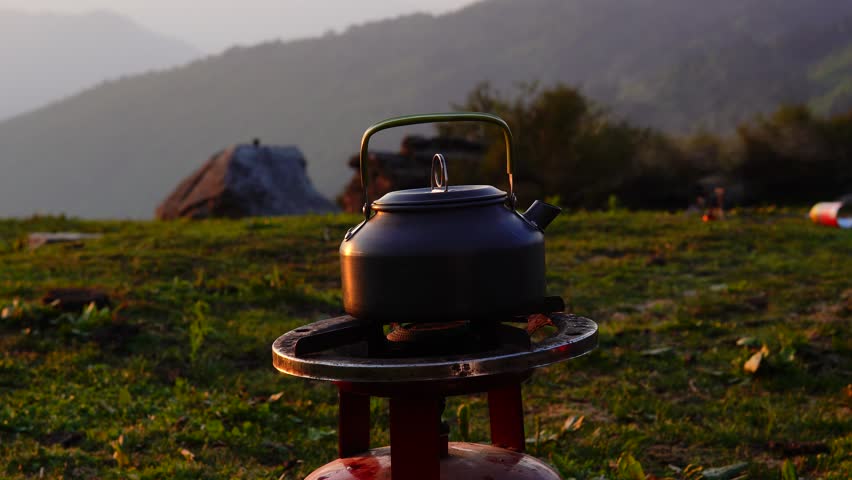 A kettle is placed on top of a gas cylinder releasing steam amidst the mountains