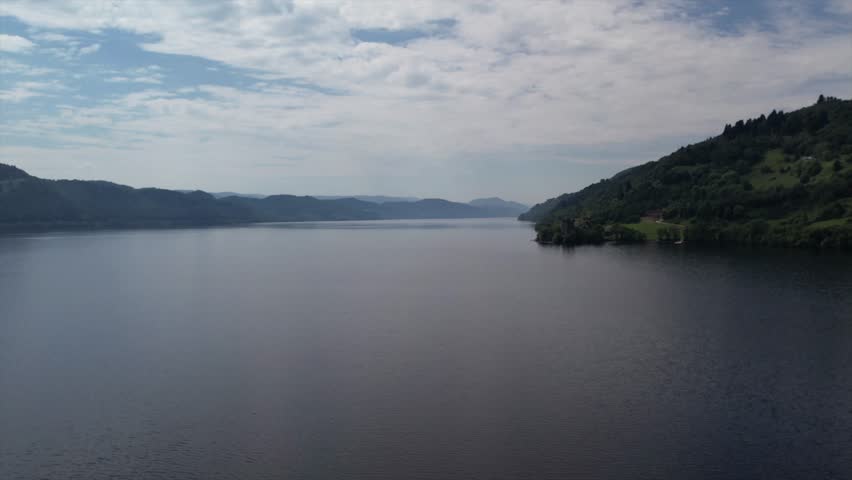 Drone footage over Loch Ness with Urquhart Castle nestled along the shoreline. Stunning views of the vast loch surrounded by the dramatic Scottish Highlands.