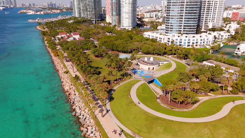 Miami Beach, Florida, USA. Aerial drone footage flying over South Pointe Park. Scenic rocks by inlet with clear water view. Palms in the park
