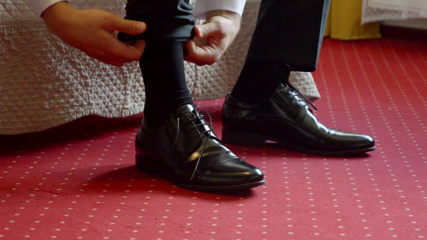 A close-up of shiny black dress shoes being laced by the groom as he prepares for the wedding