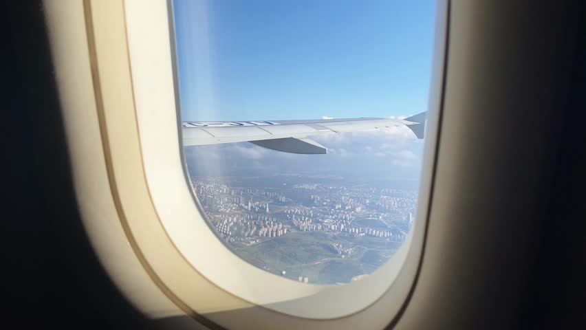 Aerial view of a sprawling urban cityscape seen through an airplane window, with a clear sky and wing visible.