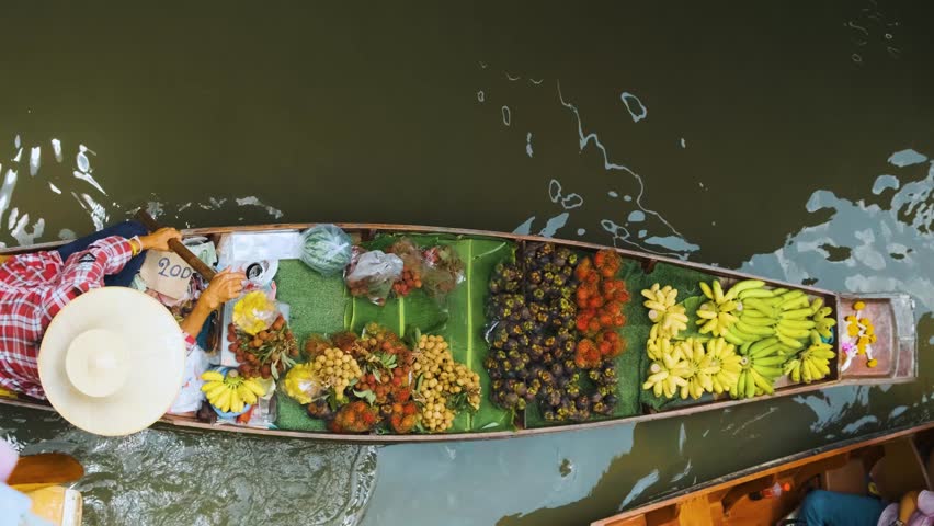 Vendor on a boat sell fresh fruits on Damnoen Saduak Floating Market near Bangkok, Thailand. Top view. Travel and touristic landmark in Asia. View from above