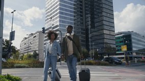 African American tourist couple holding hands crossing the busy downtown street rolling their suitcases surrounded by urban skyscrapers, wide shot. - Powered by Shutterstock - Get 15% off with code: PIKWIZARD15