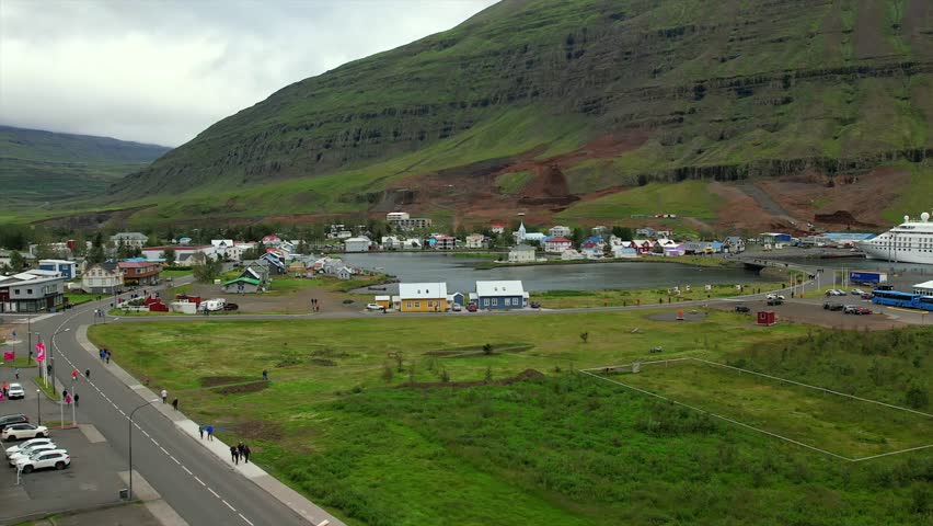 Aerial view of Seyðisfjörður, Iceland, showcasing the charming village, colorful houses, cruise ship, and lush green hillsides. Surrounded by dramatic mountains and the tranquil fjord.