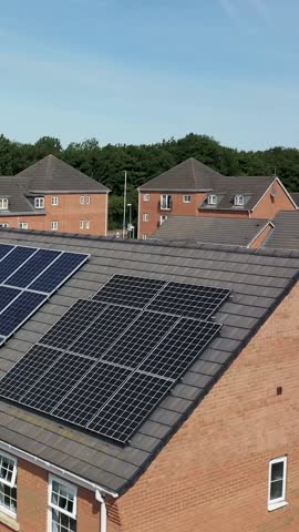 Vertical portrait aerial drone footage of a typical British newly built house with solar panels on the roof showing the drone flying across the roof taken on a sunny summers day.