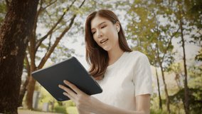 Asian Woman Working outdoors in the park. Professional on a Video Call, exploring Hybrid Work Opportunities in a Peaceful, Virtual Meeting and Online Learning. Hybrid work lifestyle concept by tablet - Powered by Shutterstock - Get 15% off with code: PIKWIZARD15