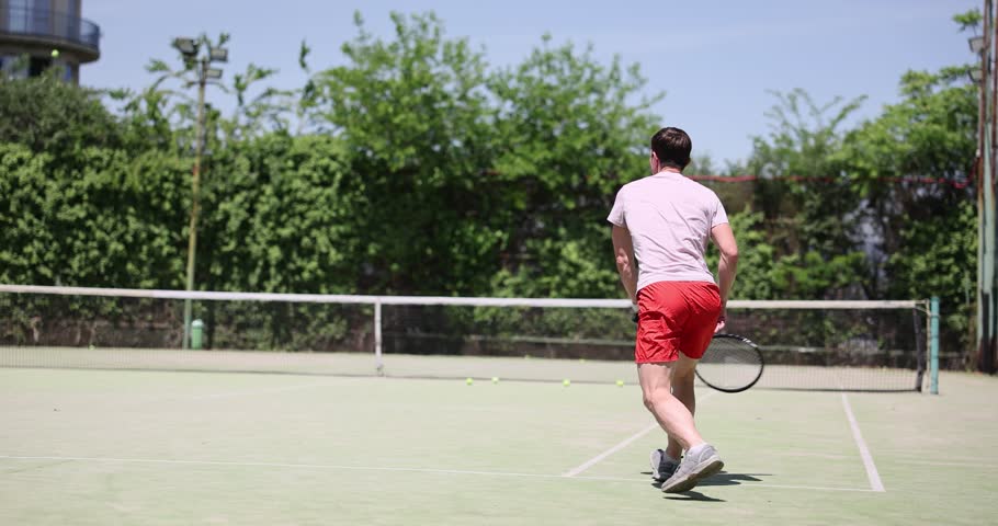 Tennis training on a sunny day with an emphasis on improving your shots off the bounce. Professionally equipped tennis player and net in background tennis player hits tennis ball with racket