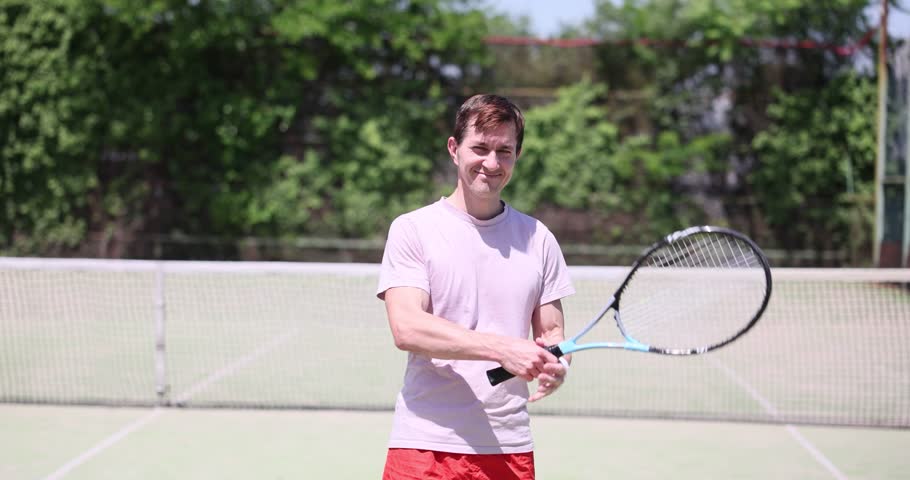 Tennis player practicing his shot on an outdoor court. Smiling male tennis player on a tennis court