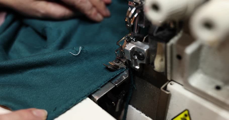 Process of sewing hem of fabric using sewing machine in workshop. Seamstress sews on sewing machine in studio