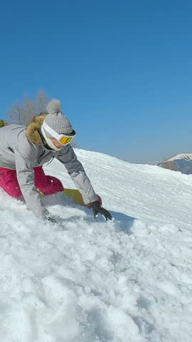 SLOW MOTION: Woman crashes into soft snow while snowboarding on snowy ski slope. Young female snowboarder tries to learn how to turn and ride snowboard at mountain ski resort on a beautiful sunny day.