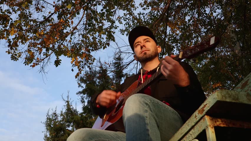 Bottom view of adult Caucasian man fingering strings at guitar. Sunny light. Learning to play a musical instrument