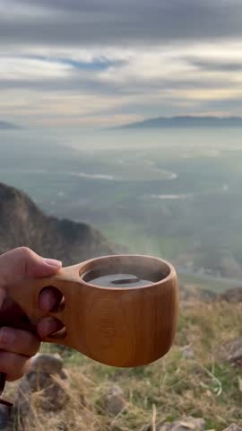 A cozy moment captured from a high-altitude viewpoint, holding a wooden cup of coffee amidst the dreamy fog and endless hills.