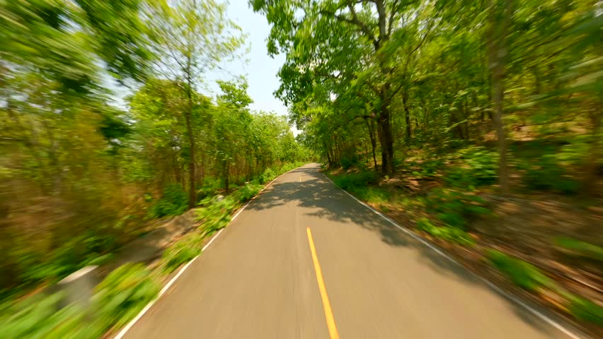 Fast FPV drone flight over the road through green forest on a sunny summer day, Thailand