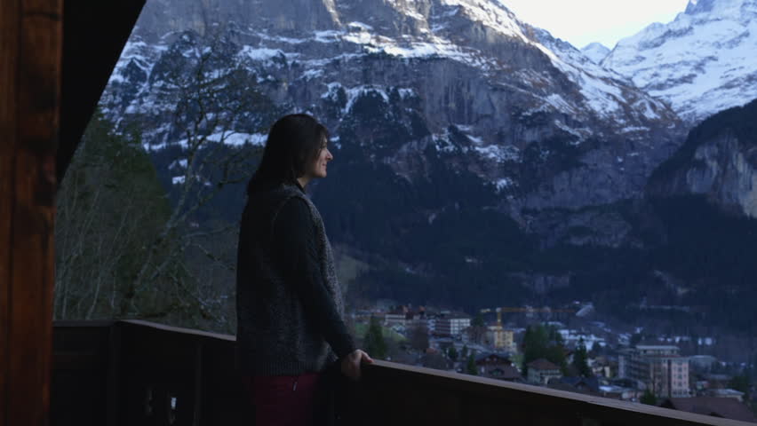 Vacationer on Swiss Alps Chalet Balcony in Winter, woman enjoys view of Mountain view in Switzerland. contemplative pensive emotion