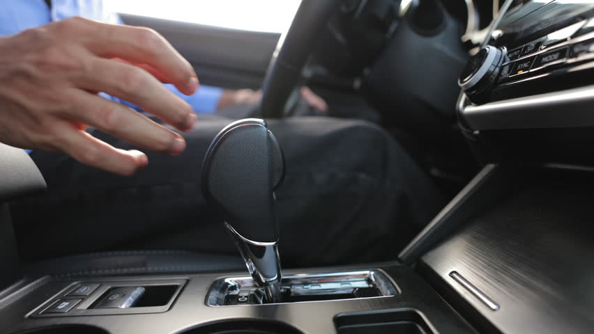 Close up of male hand shifting gears on automatic transmission inside luxury car. Crop view of anonymous man in blue shirt, with hand on gear shift, turn on drive gear. Concept of transport, comfort.