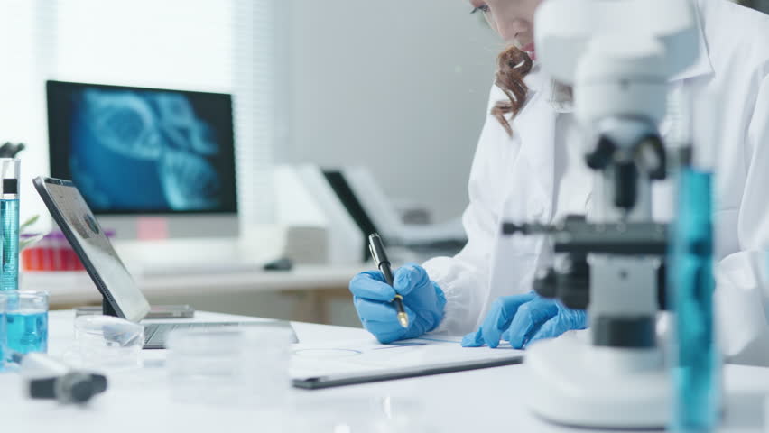 Female scientist writing notes for experimental results test biological from microscope and checking chemical at a test tube for research on pharmacy medical for and antibody for disease and virus
