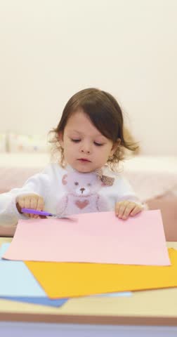 little child girl cuts colored paper with scissors at the table. kids creativity.