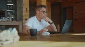 Happy businessman using laptop computer, entrepreneur working remotely from cozy wooden cottage in the mountains, enjoying morning coffee. Smiling mature man on getaway in cabin. - Powered by Shutterstock - Get 15% off with code: PIKWIZARD15