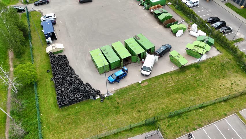 Aerial view of a recycling center with green containers, parked vehicles, and a pile of tires.