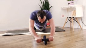 Handsome middle aged man doing exercise with abs wheel on mat. Athletic man in sportswear doing fitness workout in living room at home. Bodybuilding, fitness workout, healthy lifestyle concept. - Powered by Shutterstock - Get 15% off with code: PIKWIZARD15