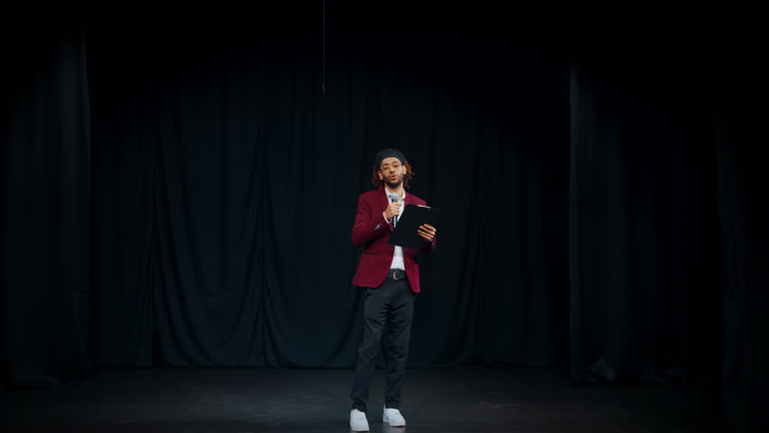 Host of award presentation standing on stage and reading speech, full-length. Handsome charismatic african man performing in concert hall or theatre, portrait on stage, talented performer of stand-up