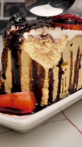 Vertical: A shiny spoon cuts off a portion of a delicious mousse cake in a plate with fresh berries and liquid melted chocolate. Souffle and berry dessert. Creamy chocolate mousse