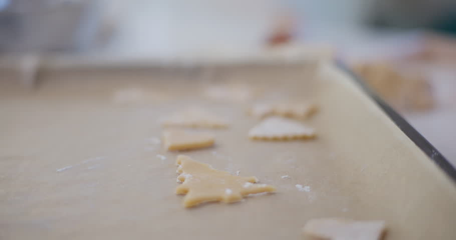 A young boy carefully arranges cut-out holiday cookies on a baking tray, preparing them for baking in the oven.