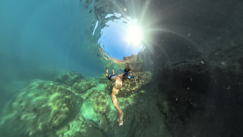 An underwater scene with a diver swimming through a tunnel of rocks, illuminated by sunlight from above, creating a serene and immersive aquatic environment.