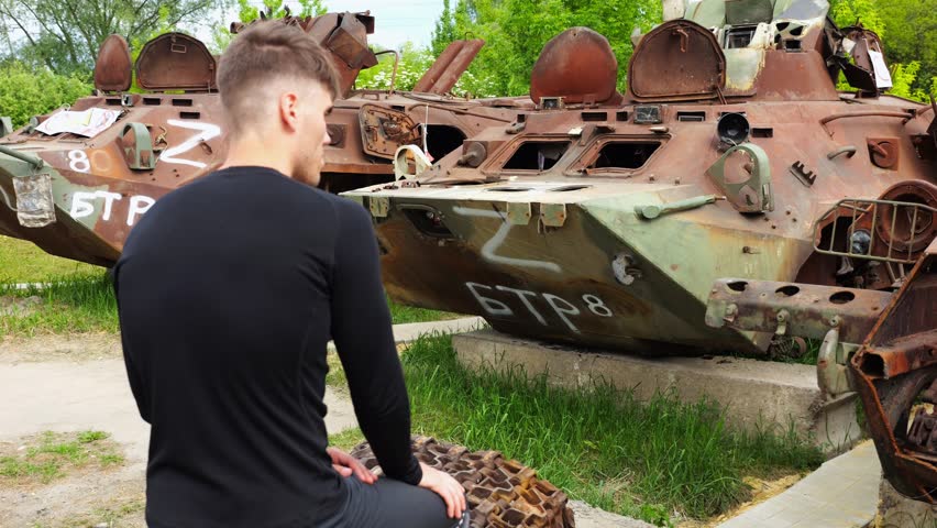 Young man looking at destroyed military equipment of the russian army. Exhibition of rusty and burned-out armored vehicles on ukrainian territory. War between Ukraine and russia. Slow motion