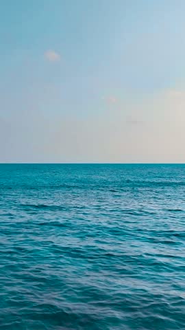 Relaxing ocean waves gently roll in under a clear sky with a calm horizon. Vertical video