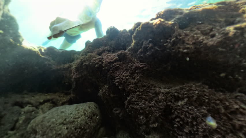 A snorkeler grabs the camera underwater, then pops to the surface through a rock opening. Sunlight filters through the water, creating a dynamic sense of motion and adventure.