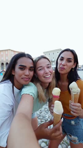 Vertical video. Diverse young women friends taking video selfie together while eating an ice cream. Multiethnic female tourist having fun on summer vacation. Female friendship concept.