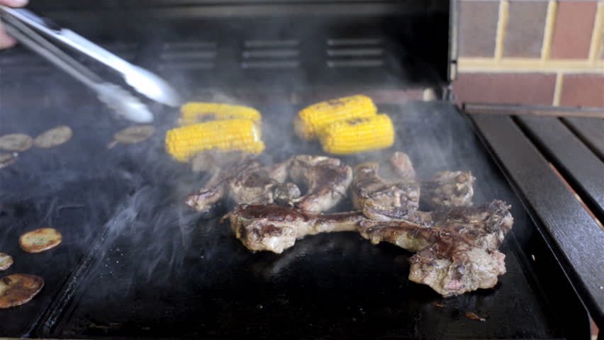 Mutton chops and corn cooking on a BBQ hot plate with lots of smoke.