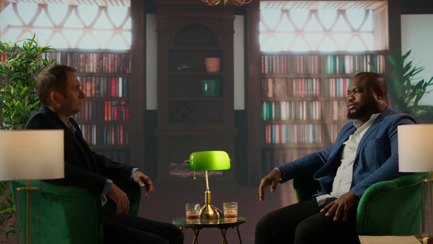 Two multiethnic businessmen sharing a whiskey glass in an elegant library, discussing business strategy and building trust. Confident gentlemen embodying luxury and elite social culture. Camera A.