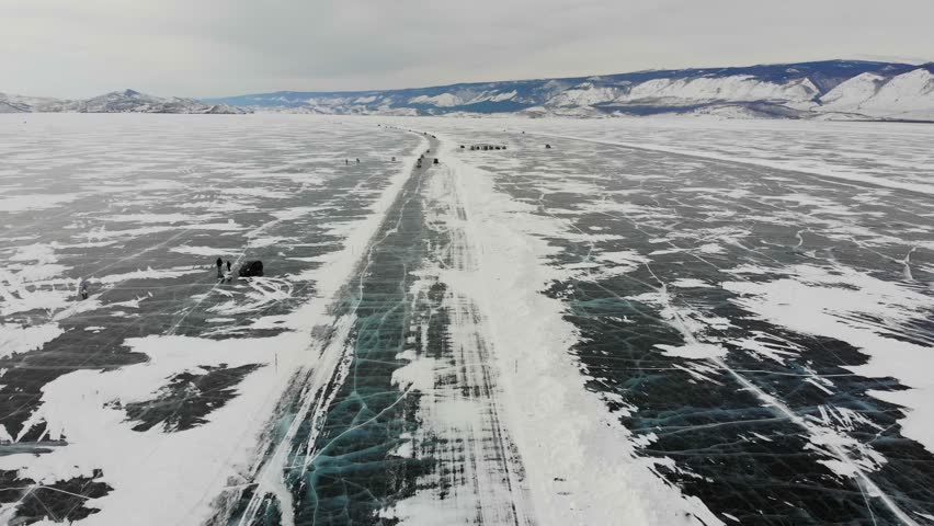 Cars drive on the ice of Lake Baikal to Olkhon Island, aerial view. Winter trip. 