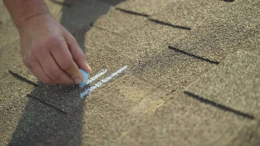 Roofer using chalk to mark hail damage on roof shingles for insurance claim photos.