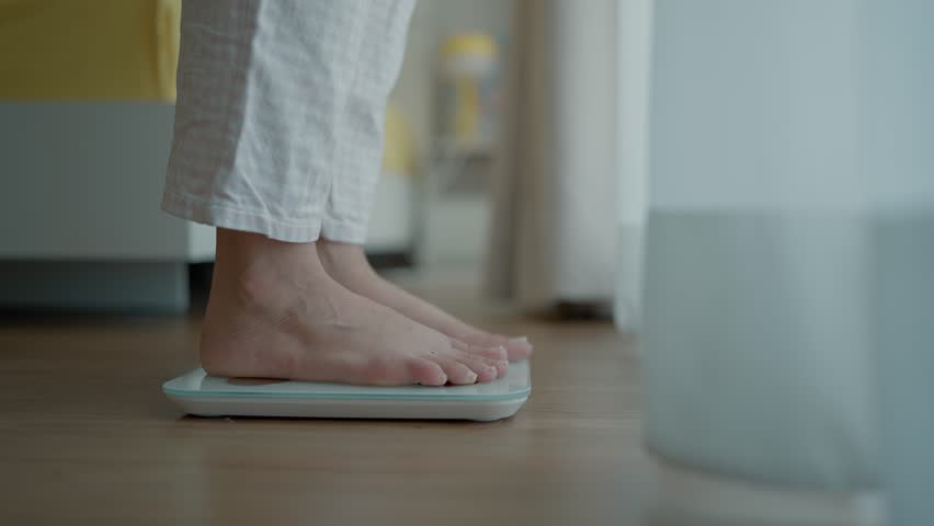 Close up a woman's bare feet stepping onto a digital weighing scale in the morning at home. Healthy lifestyle and weight awareness concept
